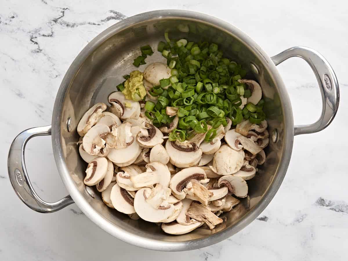 Sliced mushrooms, green onions, and grated ginger in a soup pot.