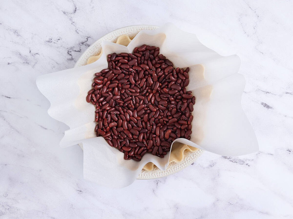 Dried beans in parchment on a pie crust for blind baking.