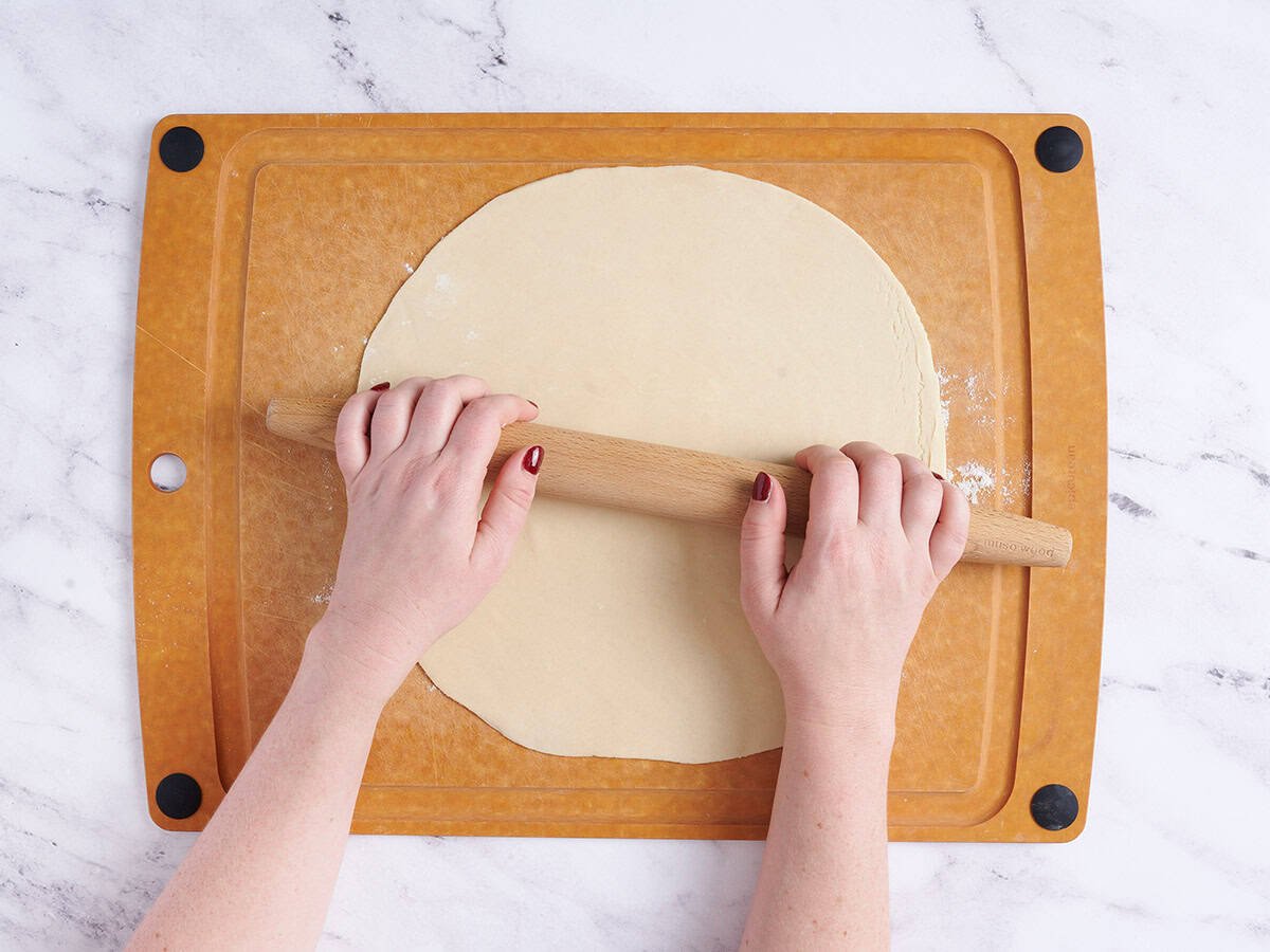 Hands using a rolling pin to roll out a pie crust.