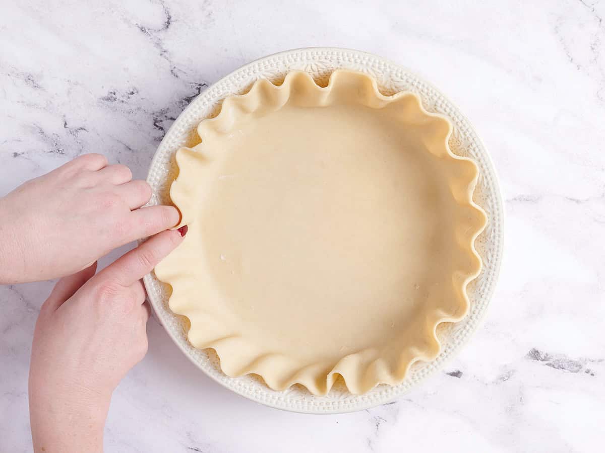 Hands crimping a pie crust.
