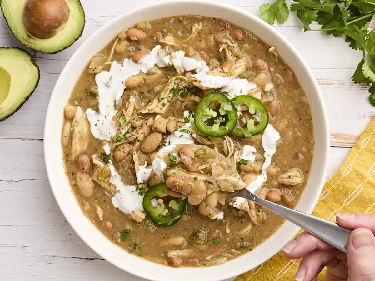 Crockpot white chicken chili in a bowl with a spoon taking some.