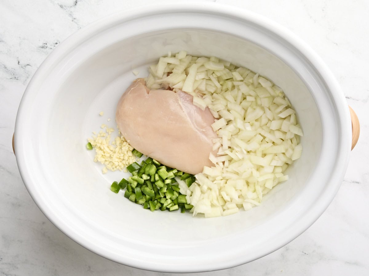 A chicken breast, minced garlic, diced onion, and jalapeno in a slow cooker.
