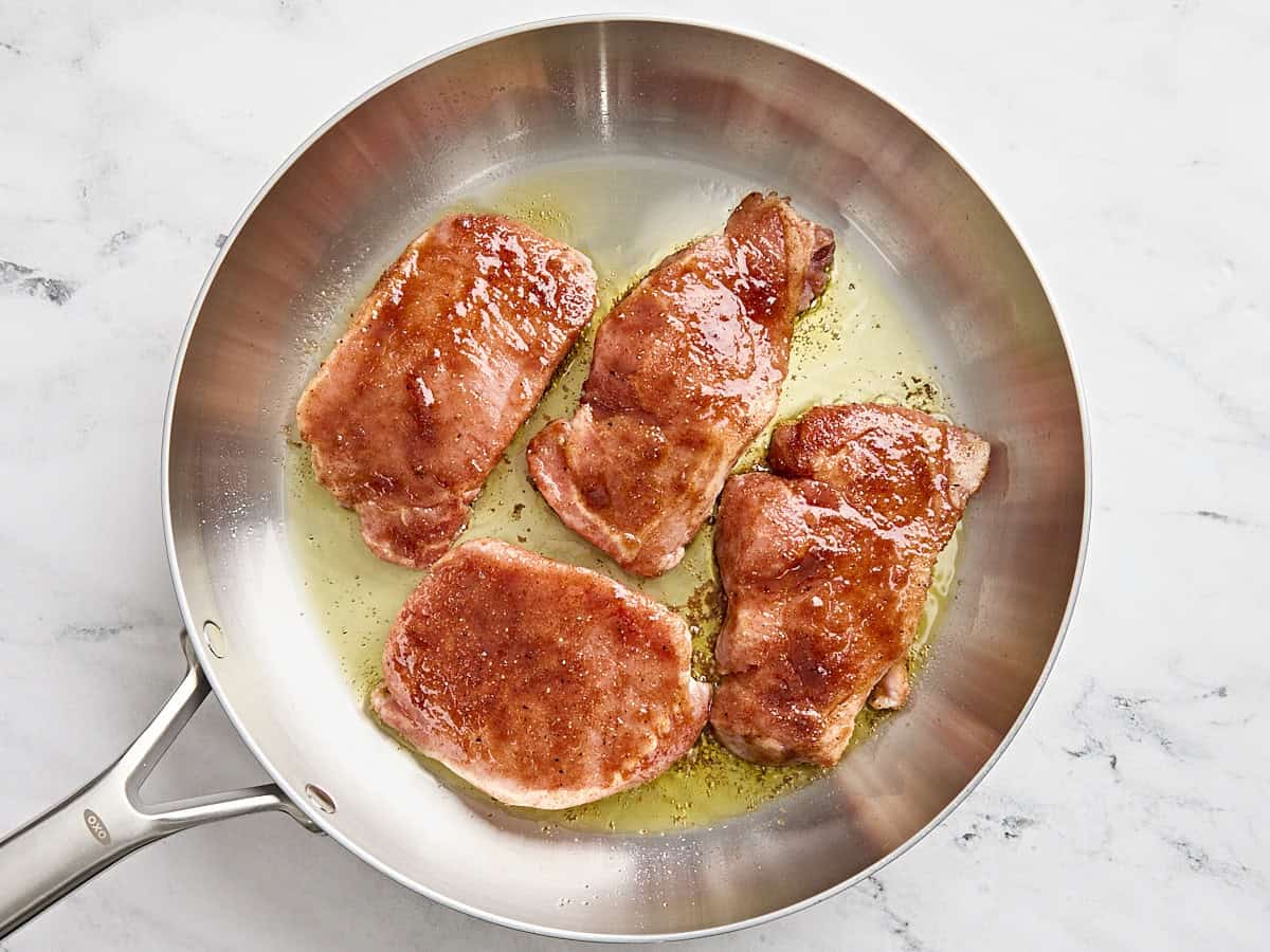 Glazed pork chops cooking in a skillet.