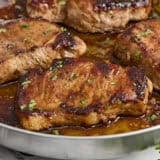 Side close up view of glazed pork chops in a skillet.