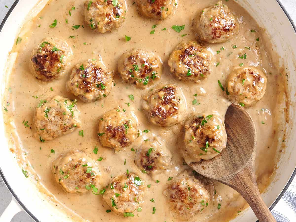 Overhead view of swedish meatballs in a skillet with a wooden spoon.