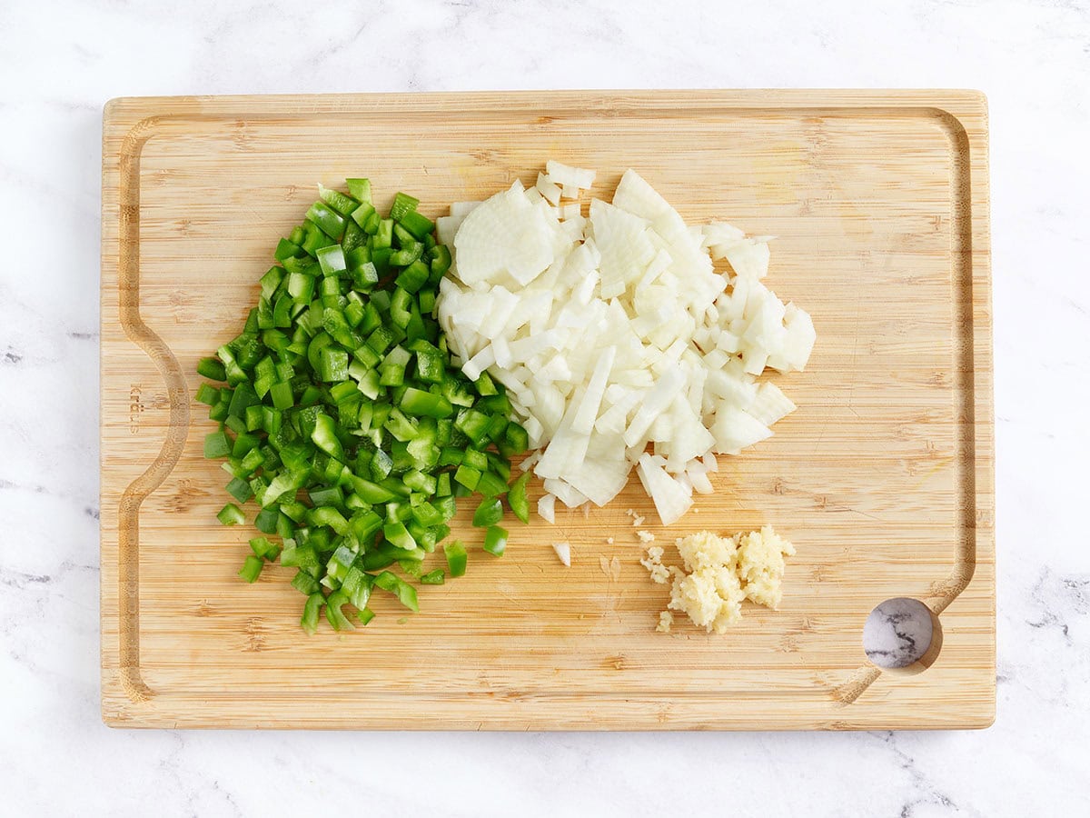 diced bell pepper and onion on a cutting board next to minced garlic