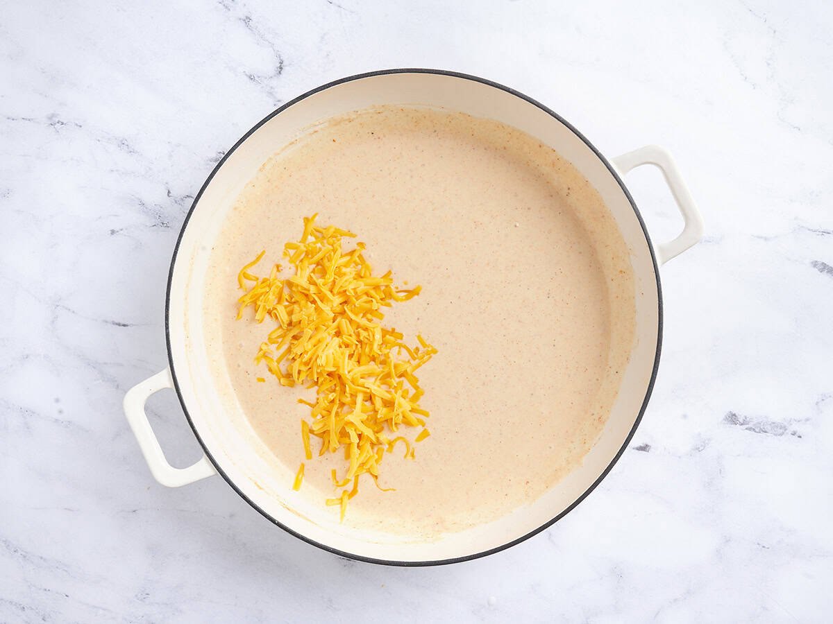 Shredded cheese added to a creamy sauce in a skillet.