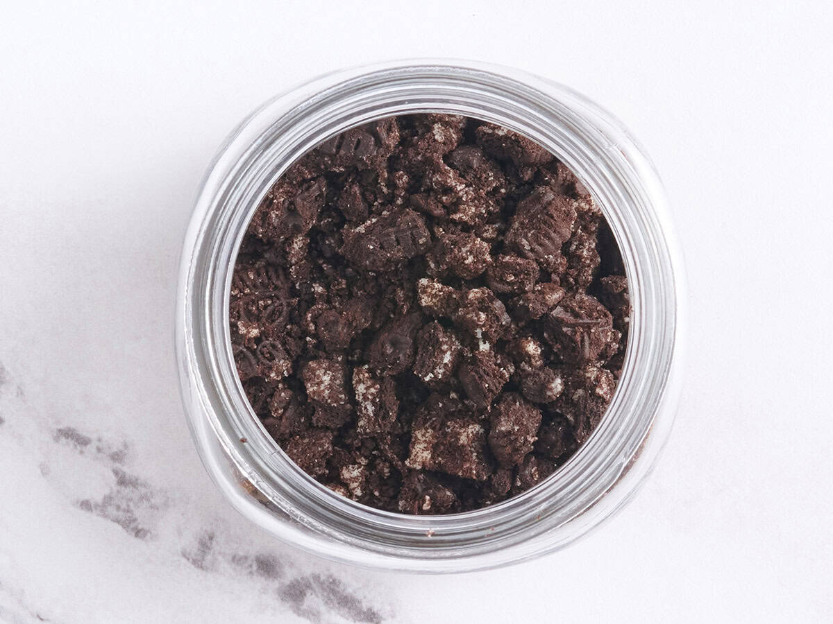 Crushed chocolate sandwich cookies added to homemade chocolate pudding in a mason jar.