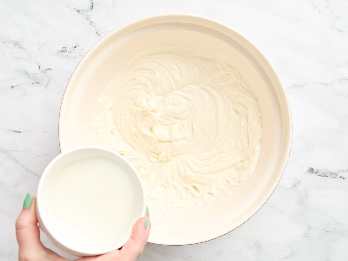 Cornstarch slurry being added to a cheesecake filling in a bowl.