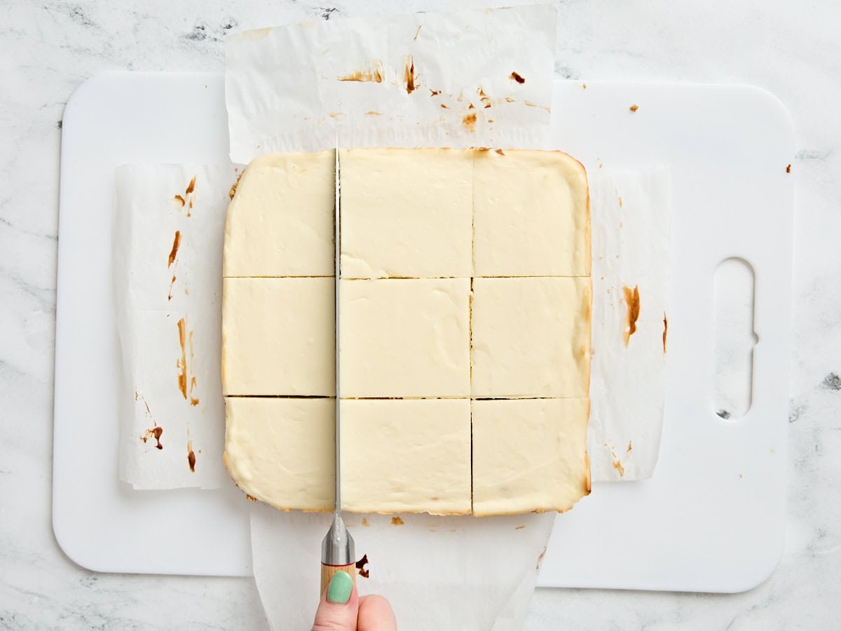 A knife slicing cheesecake bars into slices.
