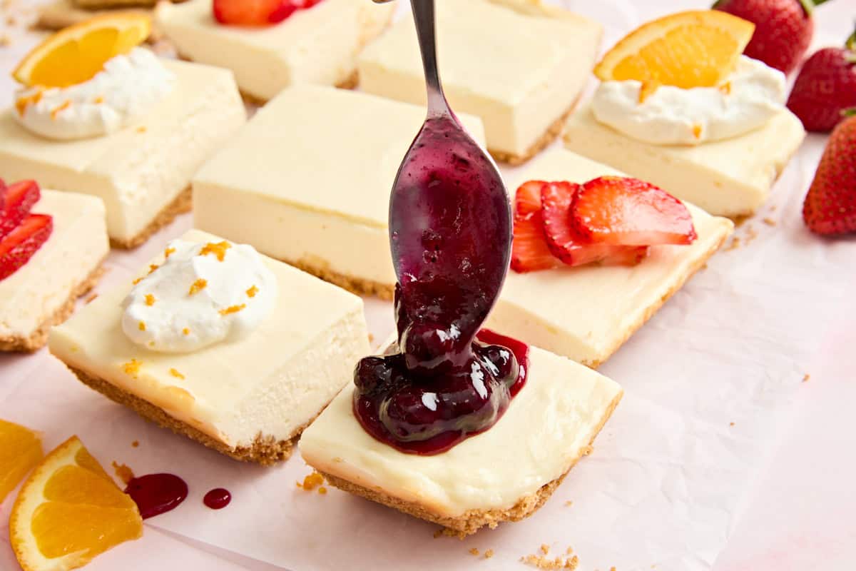 A spoon topping cheesecake bars with blueberry sauce.