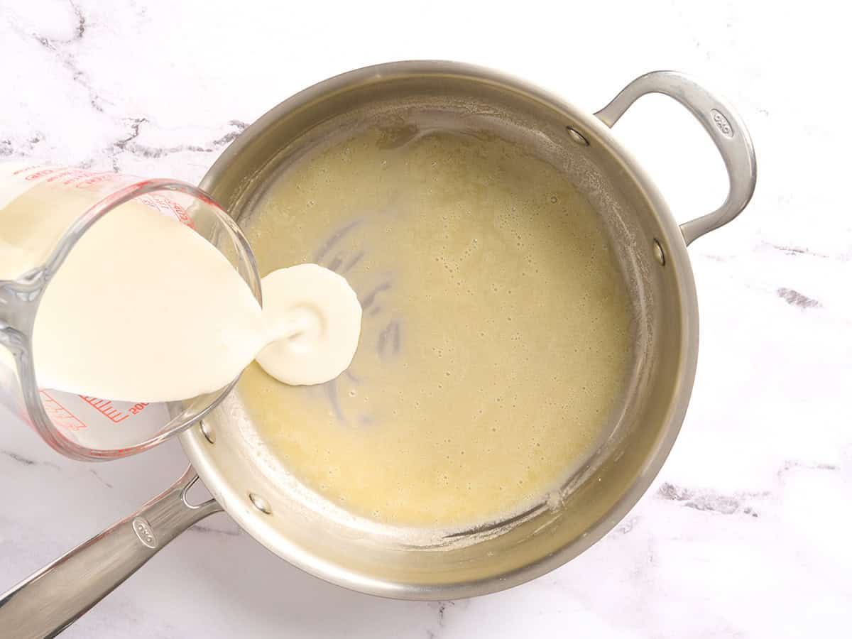 Cream being poured into a roux in a skillet.