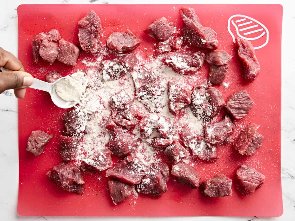 Flour sprinkled over beef stew meat on a cutting board.