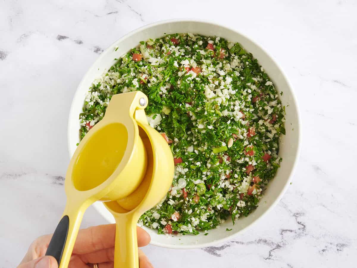 A juicer squeezing a lemon into a bowl of easy cauliflower tabbouleh.