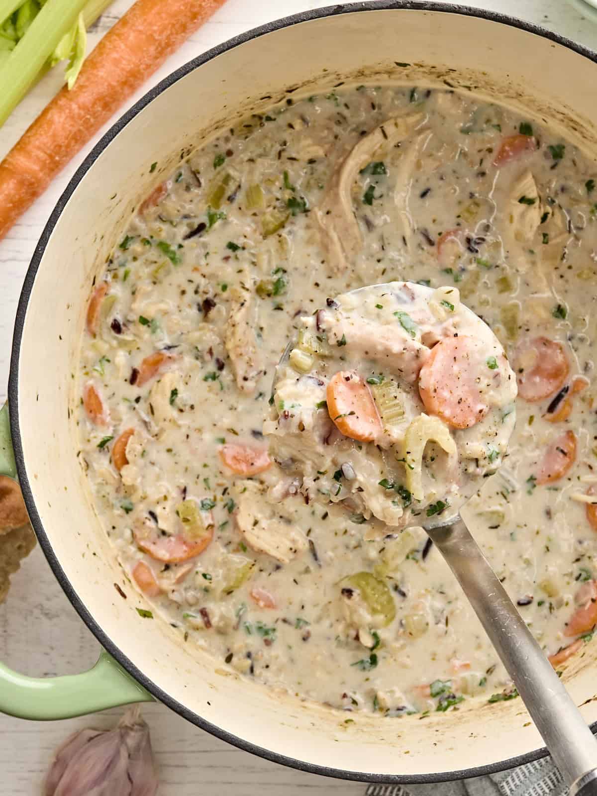Overhead view of a pot of creamy chicken and rice soup with a ladle taking some.