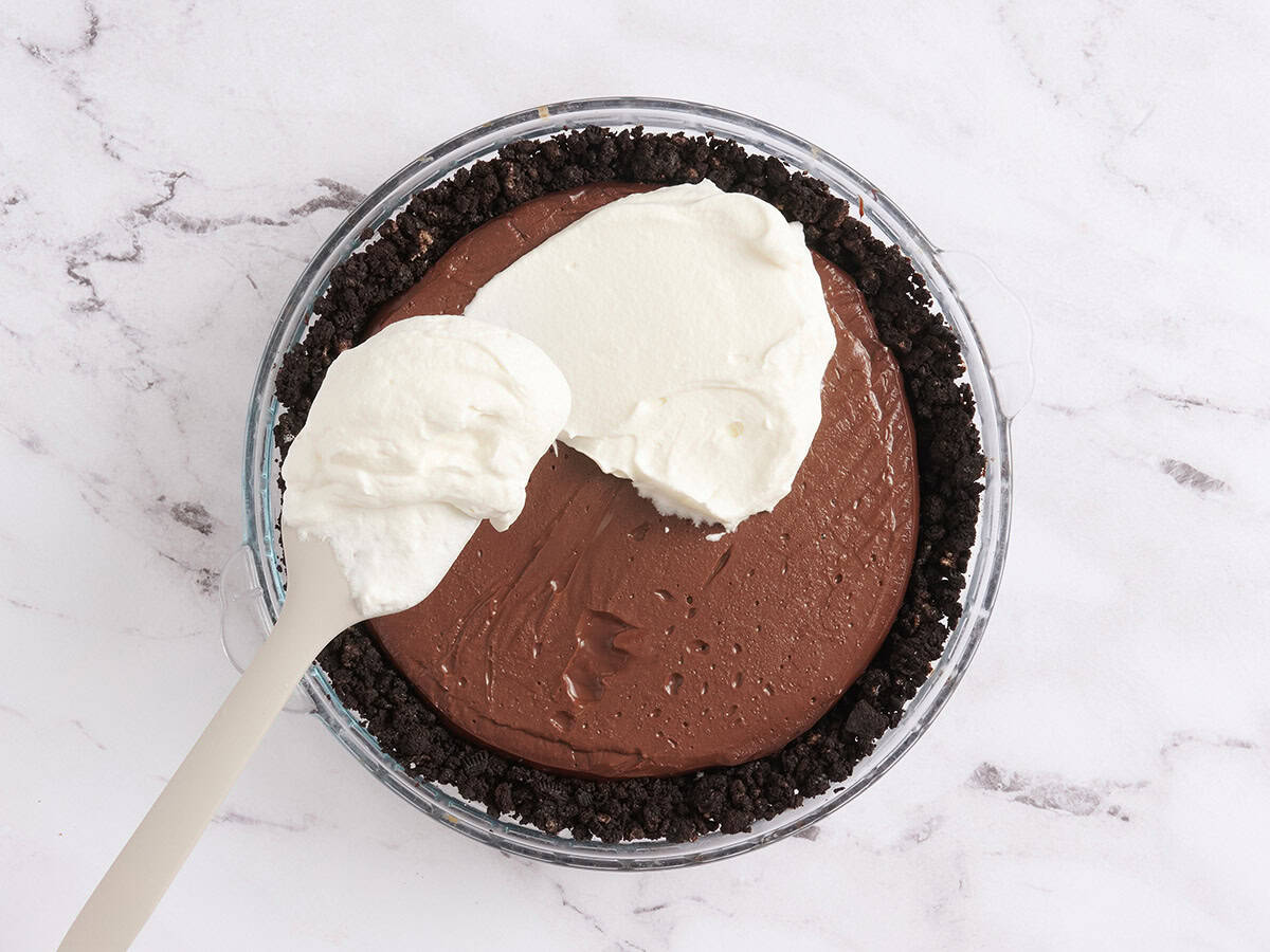 Whipped cream being spread on a Mississippi Mud Pie.