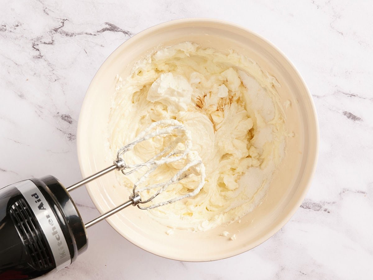 Cheesecake filling in a bowl with a hand mixer.
