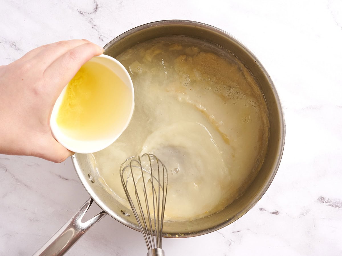 Broth being added to a creamy sauce for chicken and rice casserole in a sauce pan