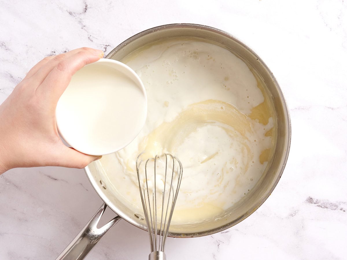 Milk being whisked into a roux in a sauce pan