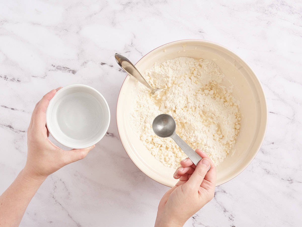 Water being added to the ingredients for pie crust in a bowl.