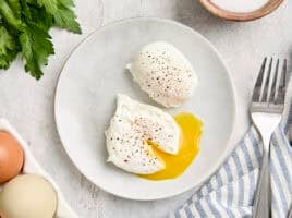 Overhead view of two poached eggs on a plate, with one cut open and the yolk running from it.