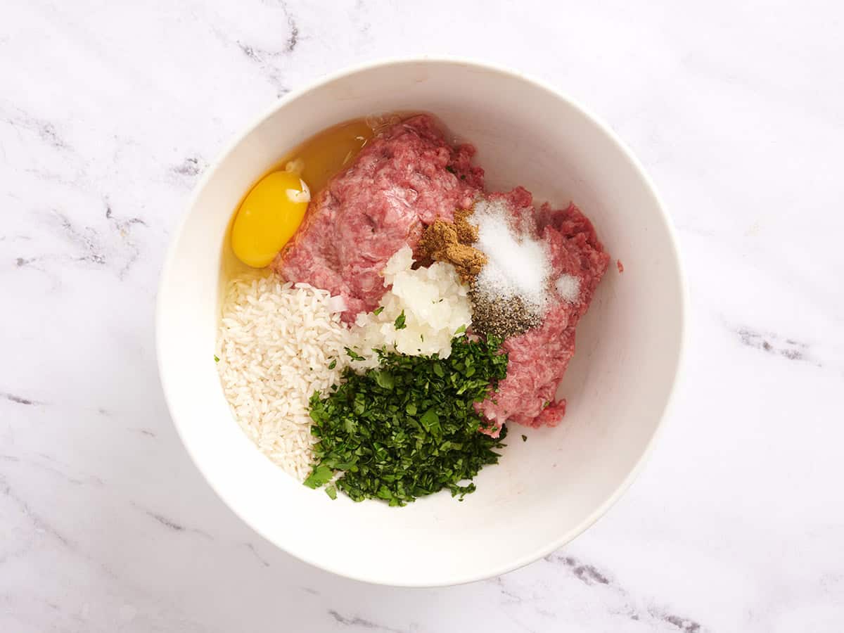 Ground beef, uncooked white rice, egg, onion, seasonings, and fresh cilantro in a mixing bowl.