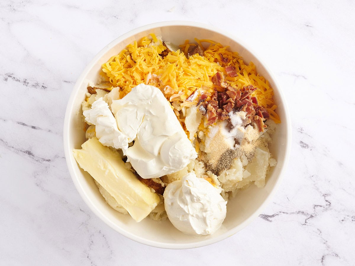 Potato, cheese, bacon, sour cream, cream cheese and butter in a bowl.