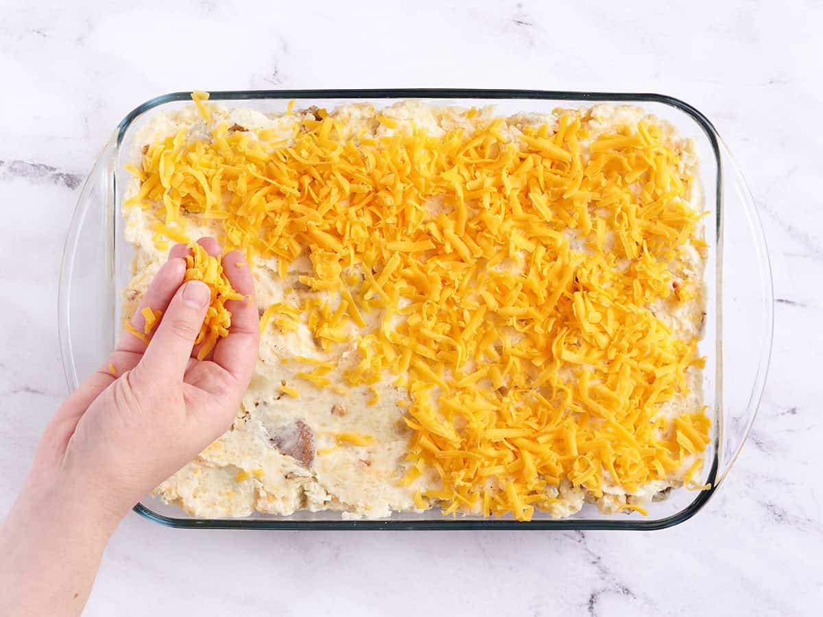 A hand topping a twice baked casserole with cheese.