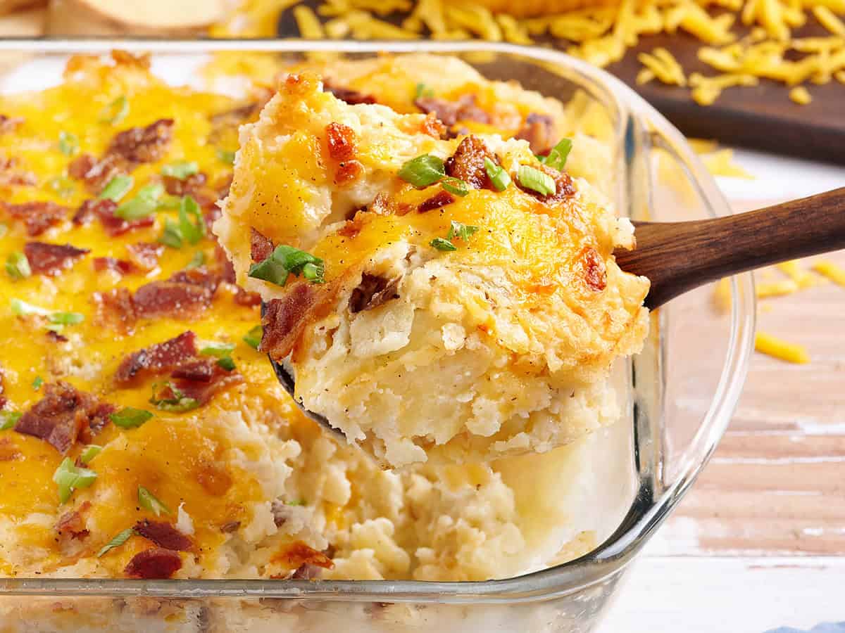 Side view of a twice baked potato casserole with a spoon taking some out the dish.