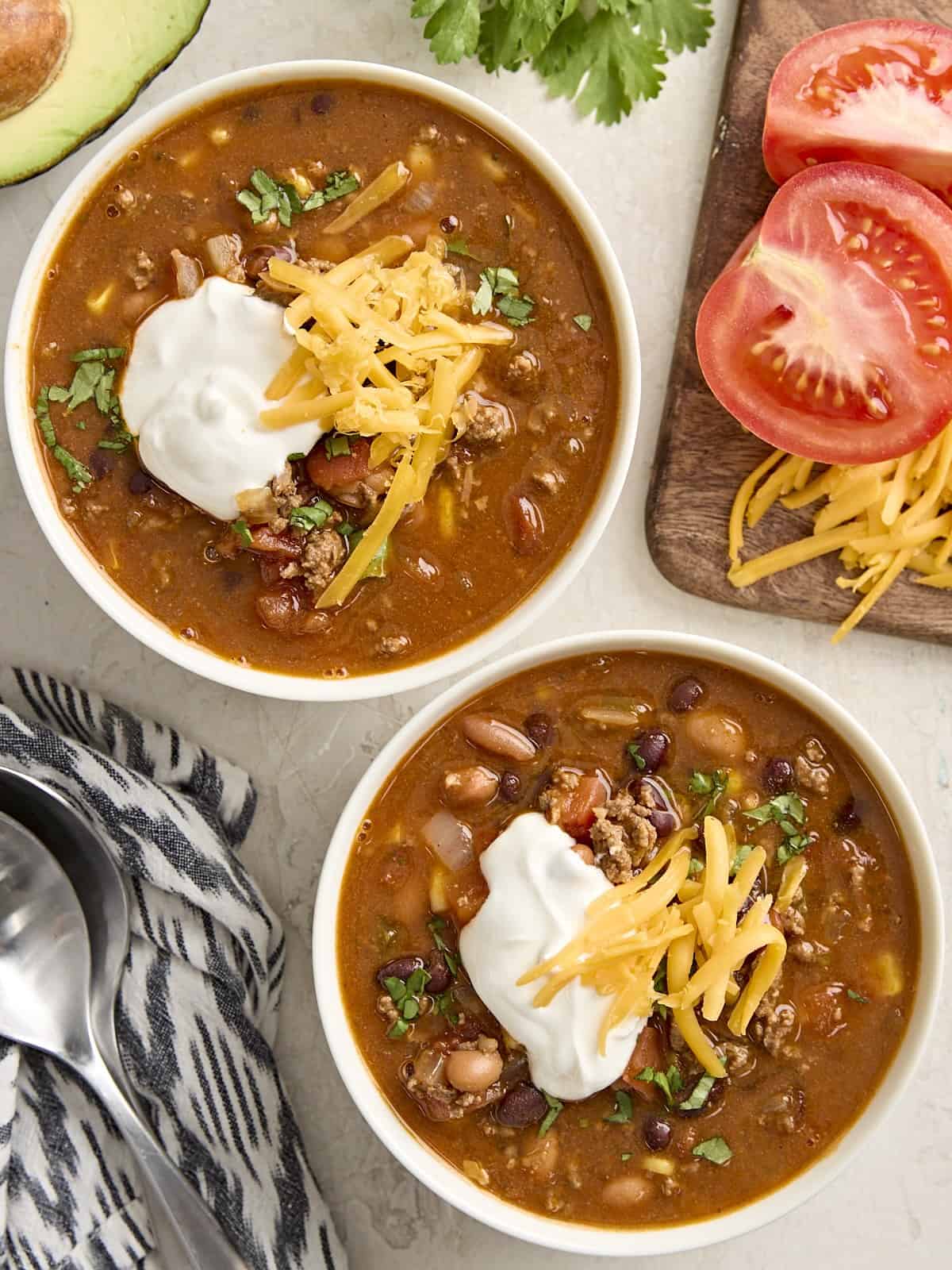 Overhead view of two bowls of taco soup, topped with sour cream and shredded cheese.