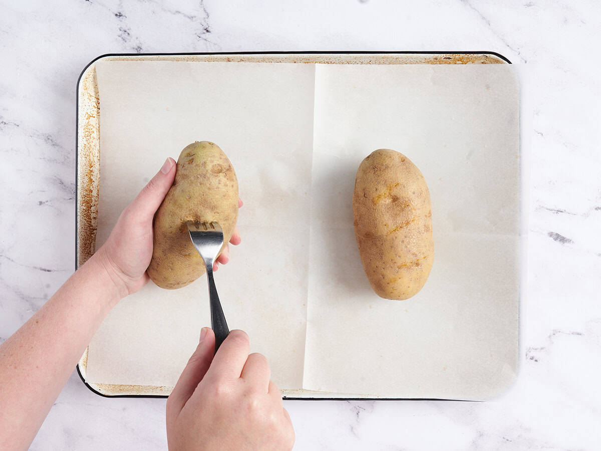 Piercing potatoes over a parchment lined baking sheet. 