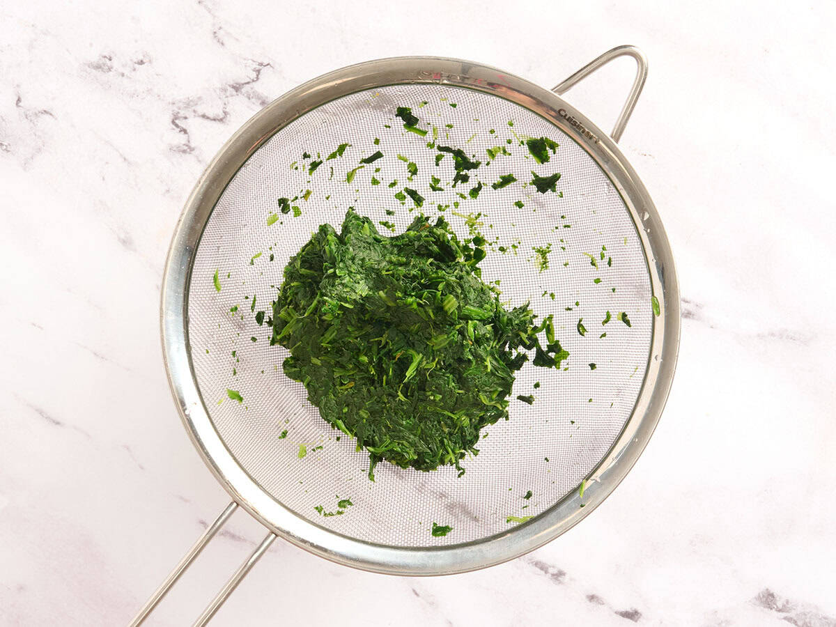 Frozen spinach in a mesh strainer.