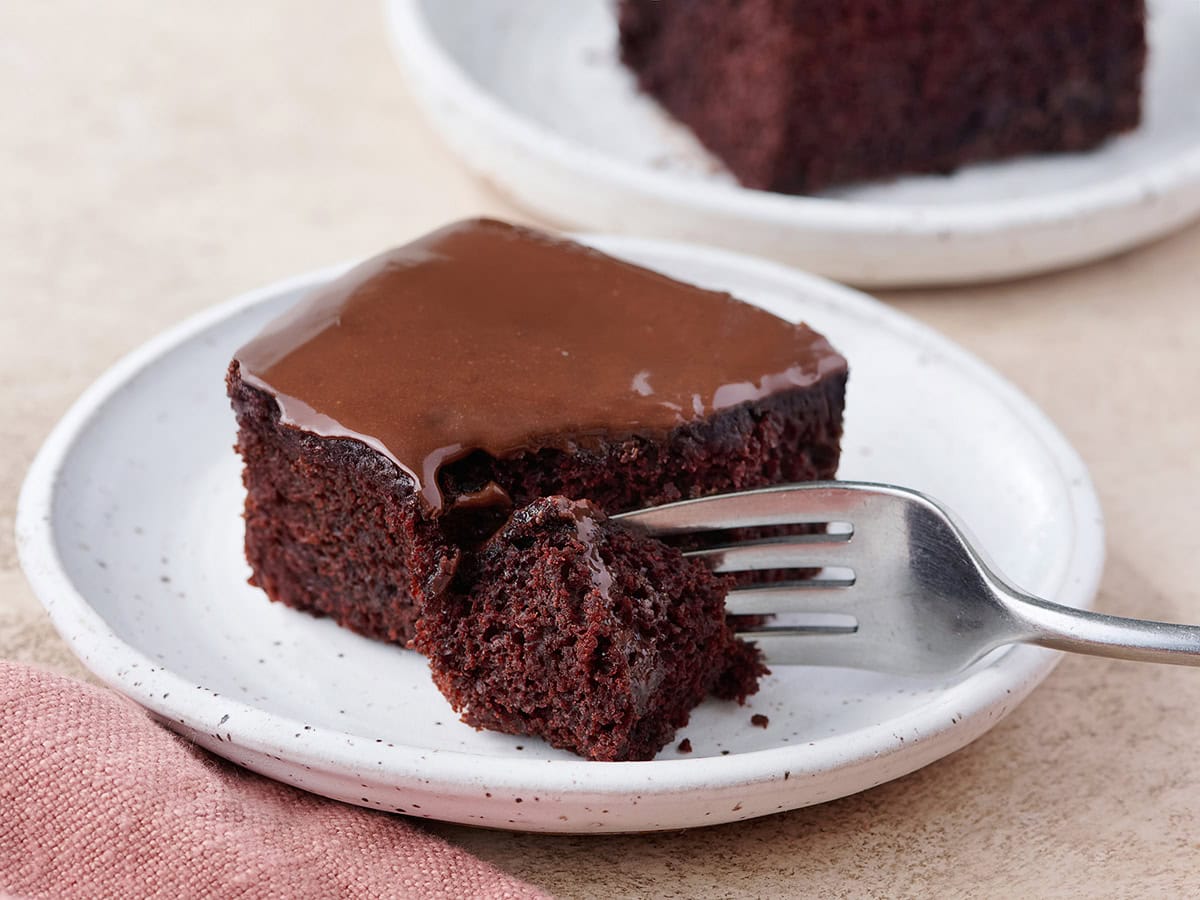 A slice of homemade chocolate depression cake on a plate with a fork taking some.