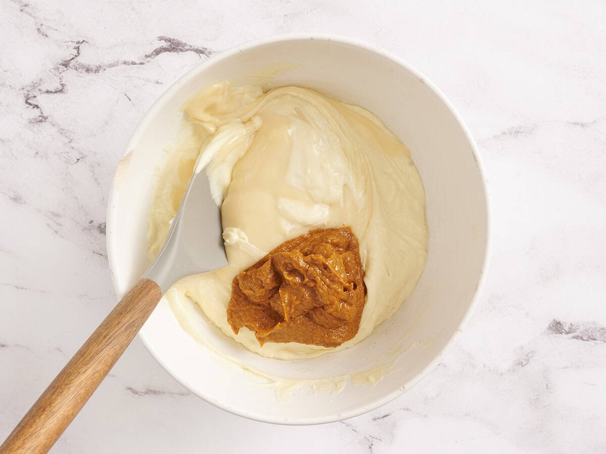 Pumpkin puree mixture added to melted white chocolate in a bowl.