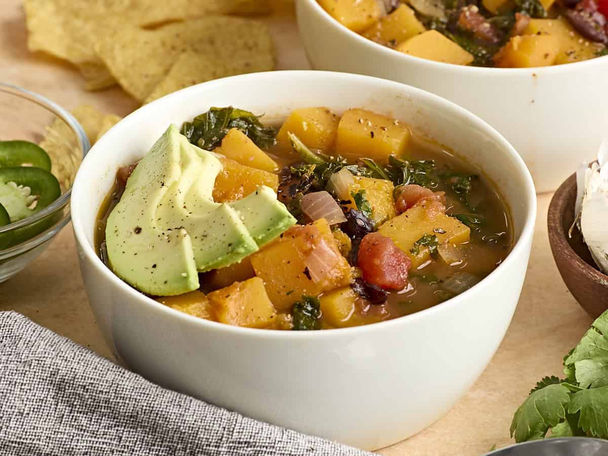 Side view of a bowl of butternut squash and black bean soup, topped with sliced avocado.