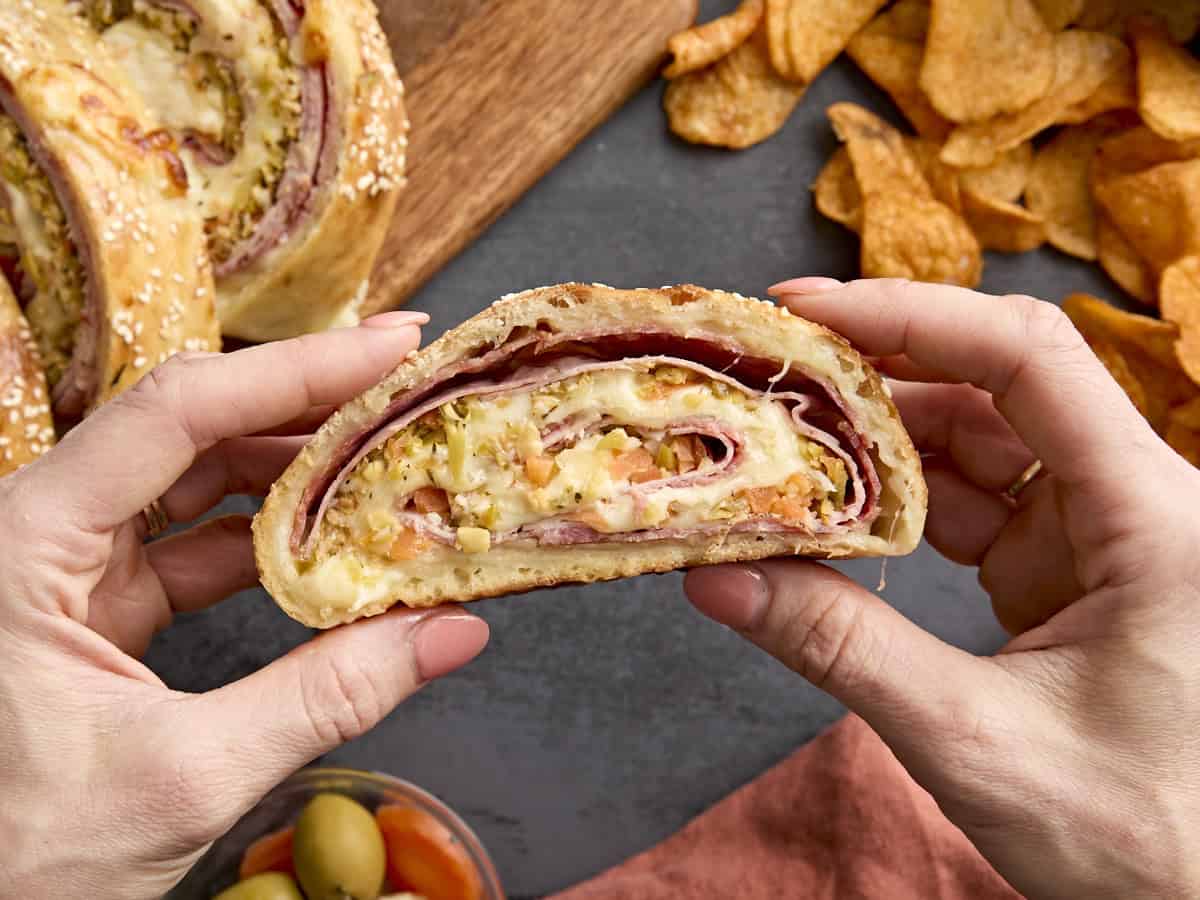 Hands holding a slice of muffaletta roll up