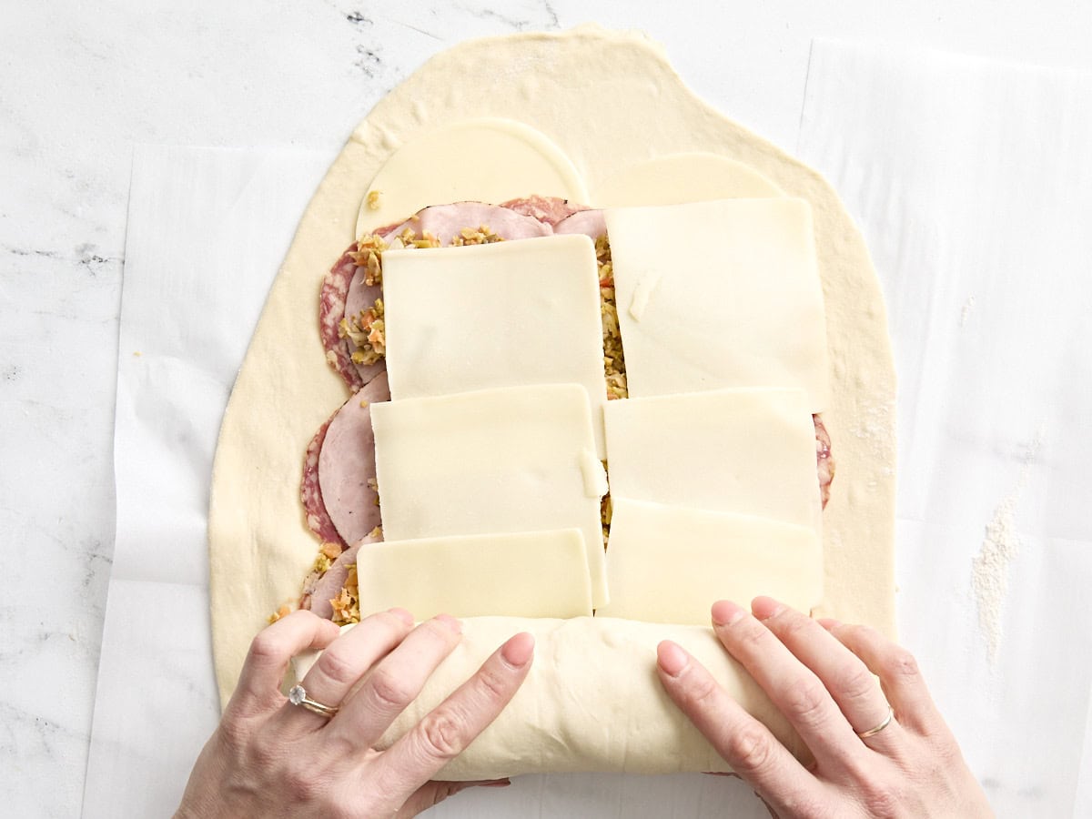 Hands rolling the pizza dough over the fillings for muffaletta roll ups