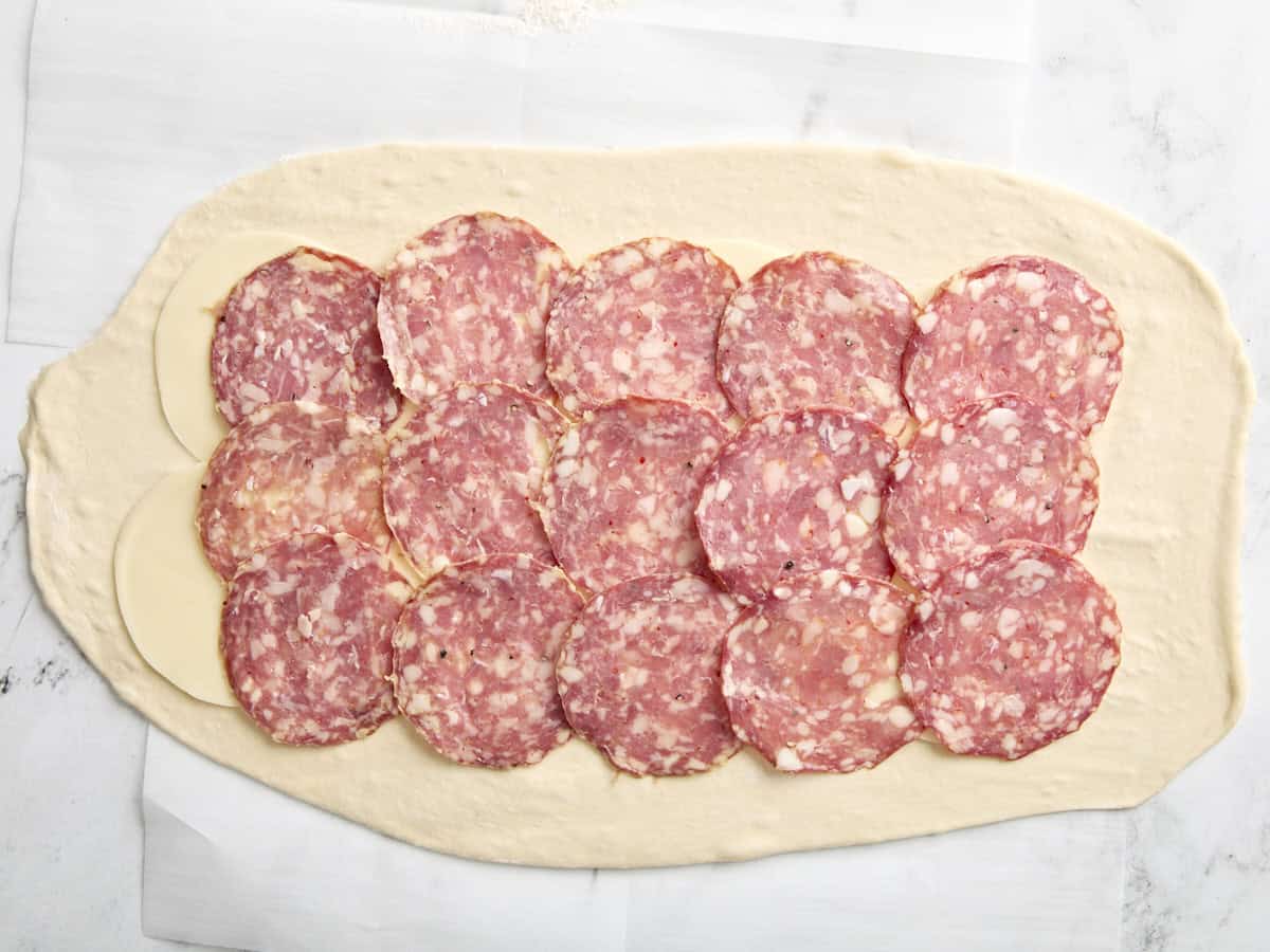 Pizza dough topped with salami slices