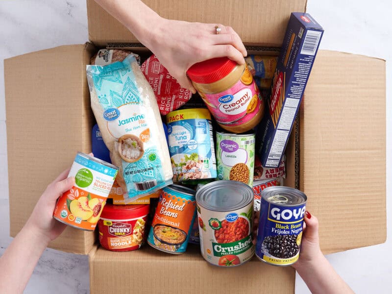 pantry items being put into a cardboard box to be donated