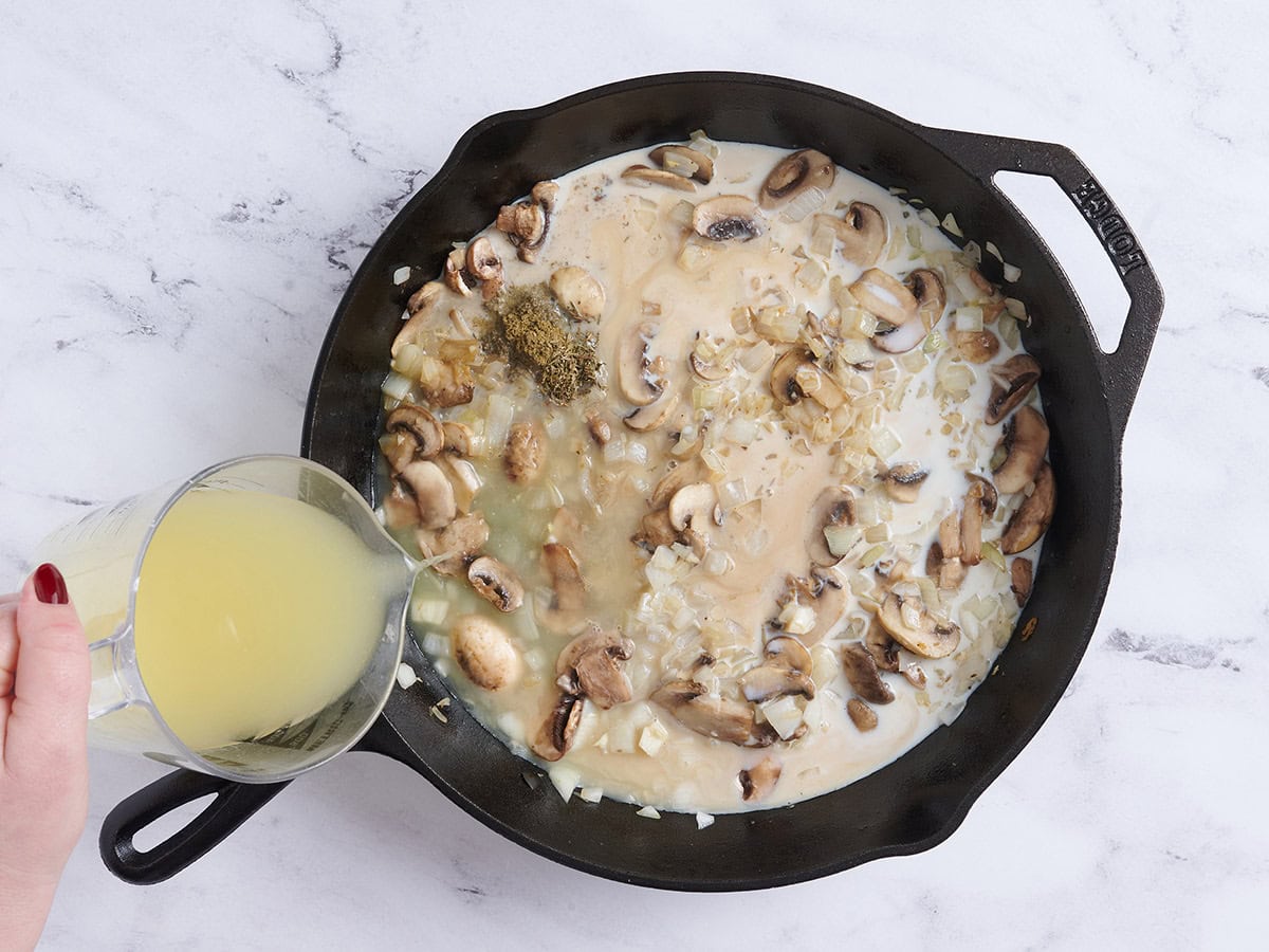 Chicken broth being poured into a skillet of chicken cobbler filling.