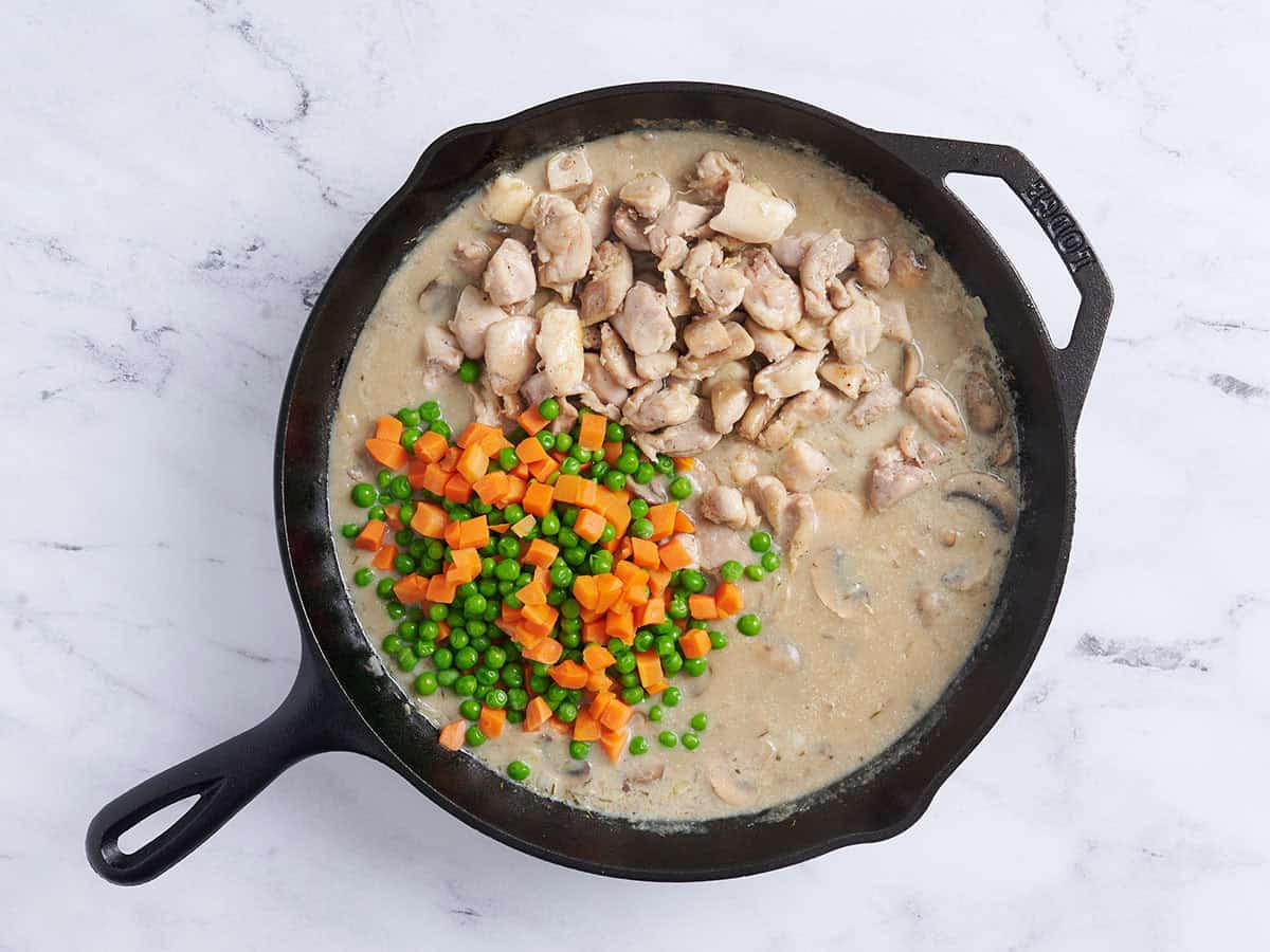 Cooked chicken pieces, carrots and peas added to a skillet.
