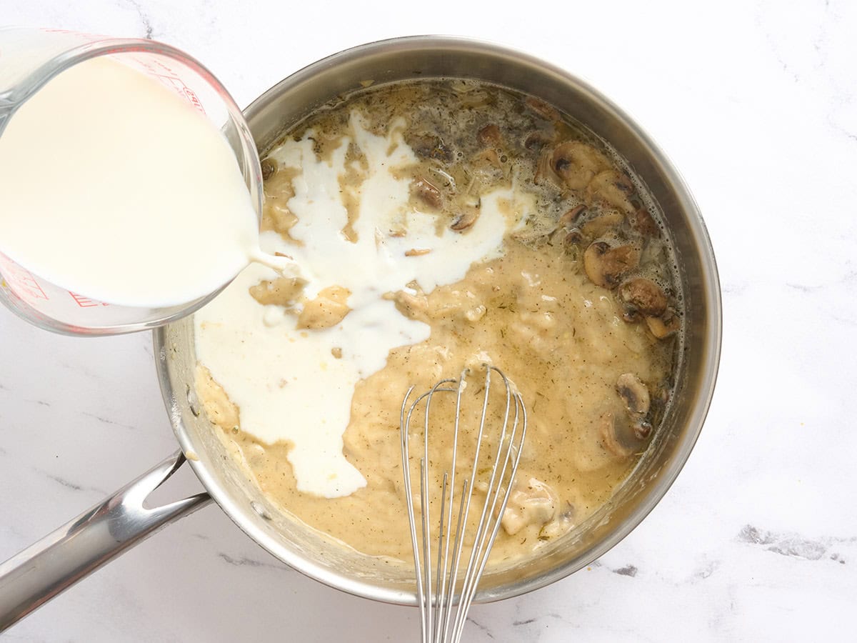 Milk being poured into a skillet with a roux.