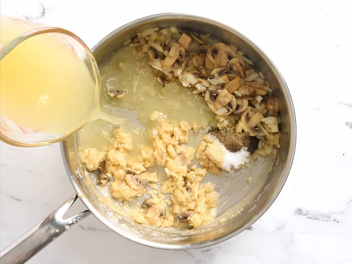 Broth added to a roux and mushrooms in a skillet.