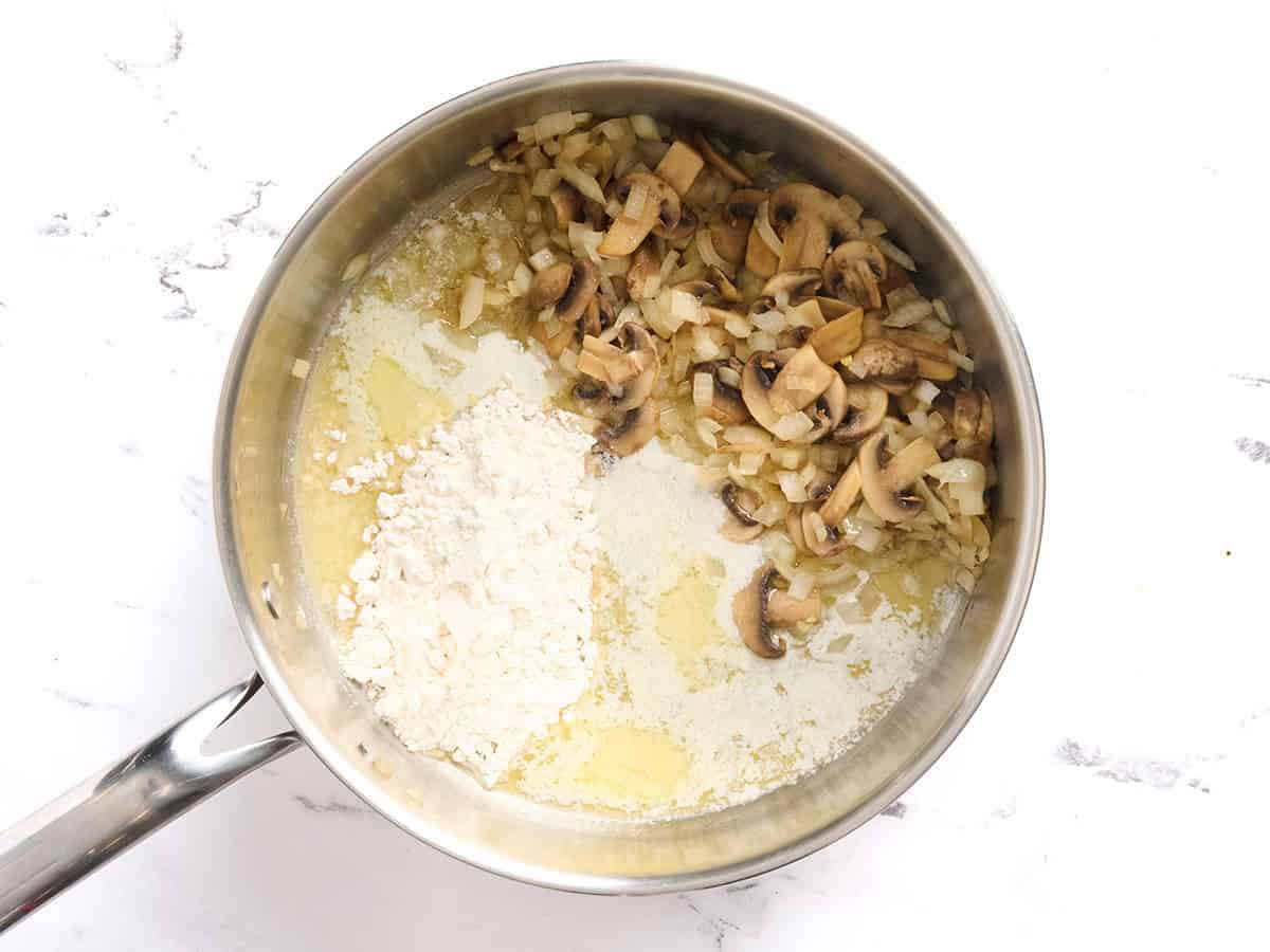 Flour and melted butter added to a skillet of sauteed mushrooms.