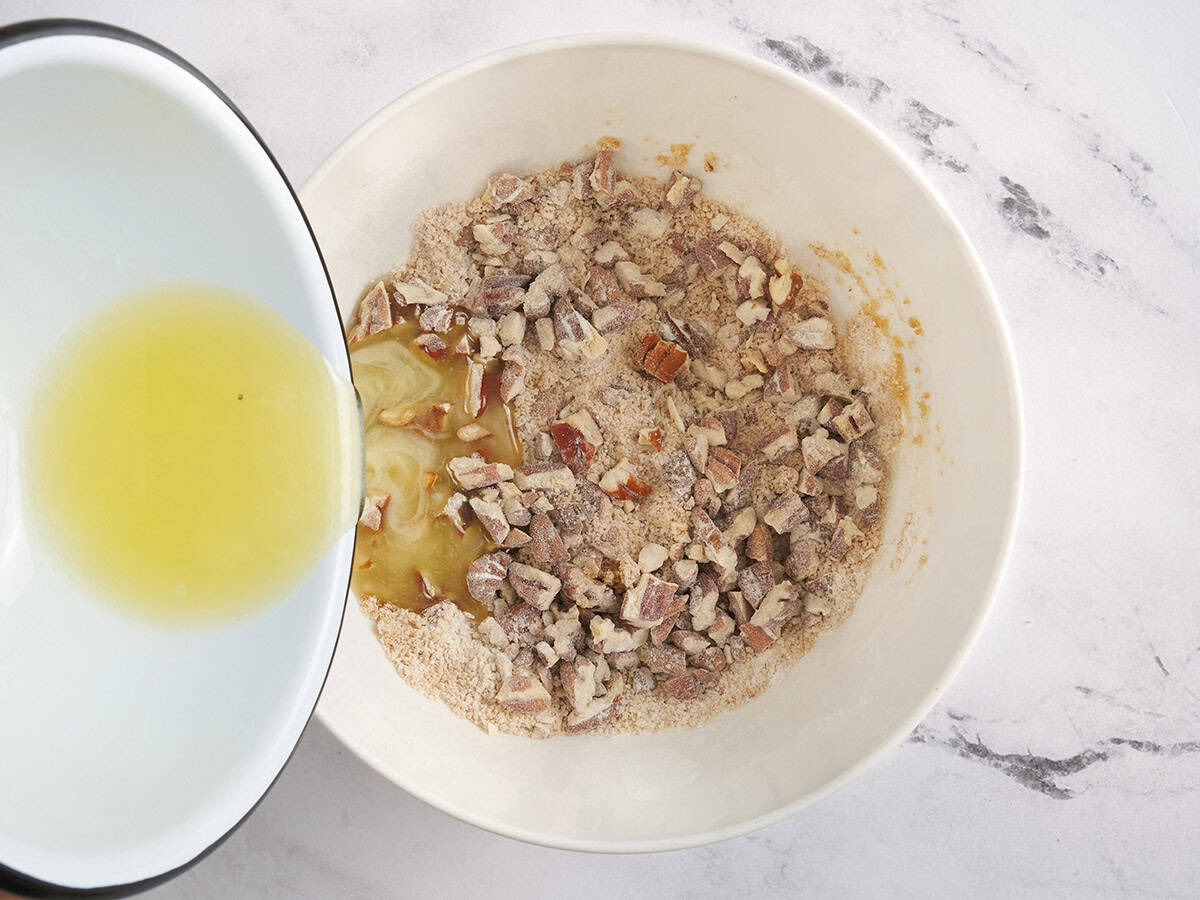 Melted butter being poured into a pecan streusel topping in a bowl.