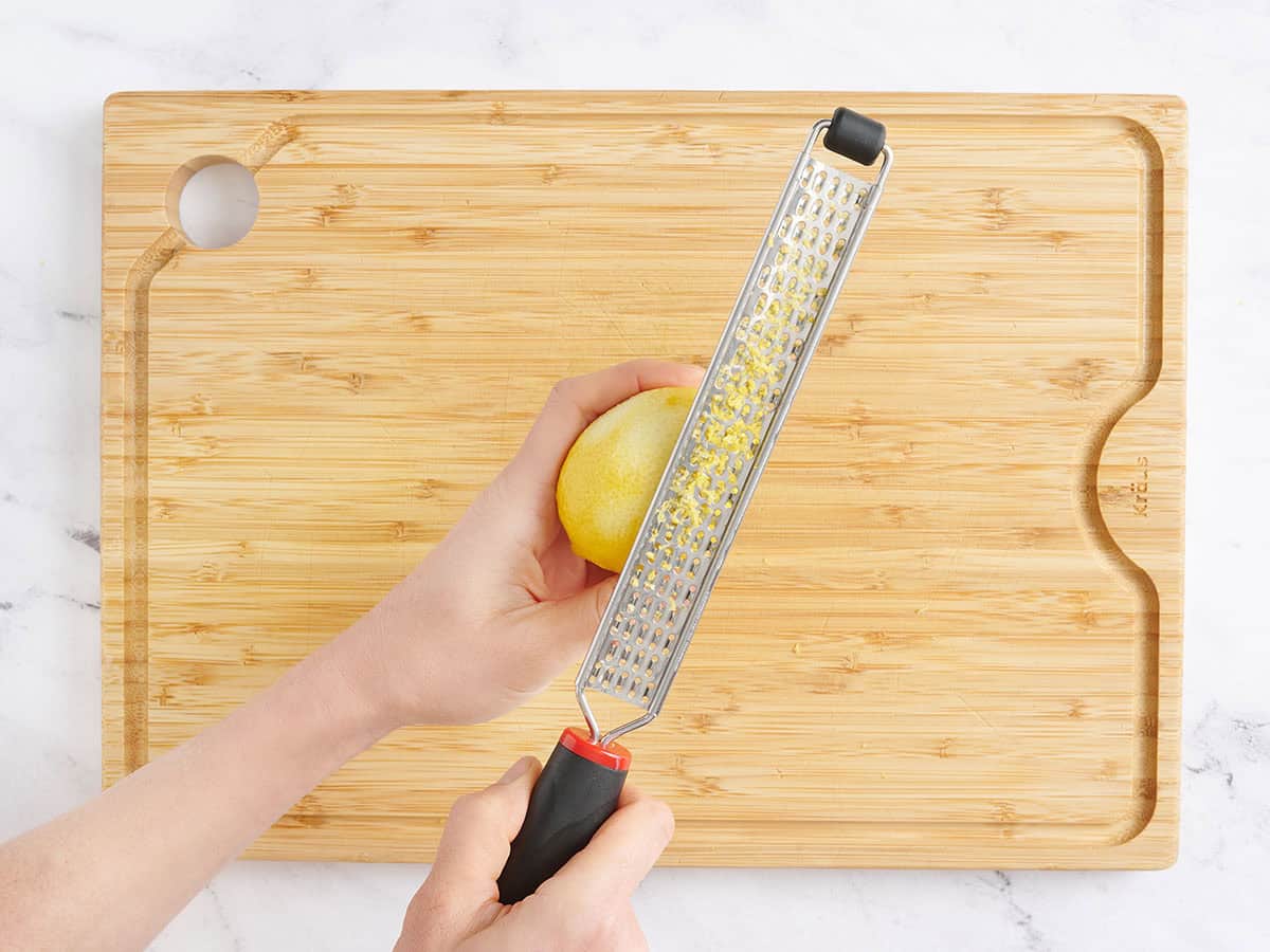 A hand using a zester to zest a lemon.