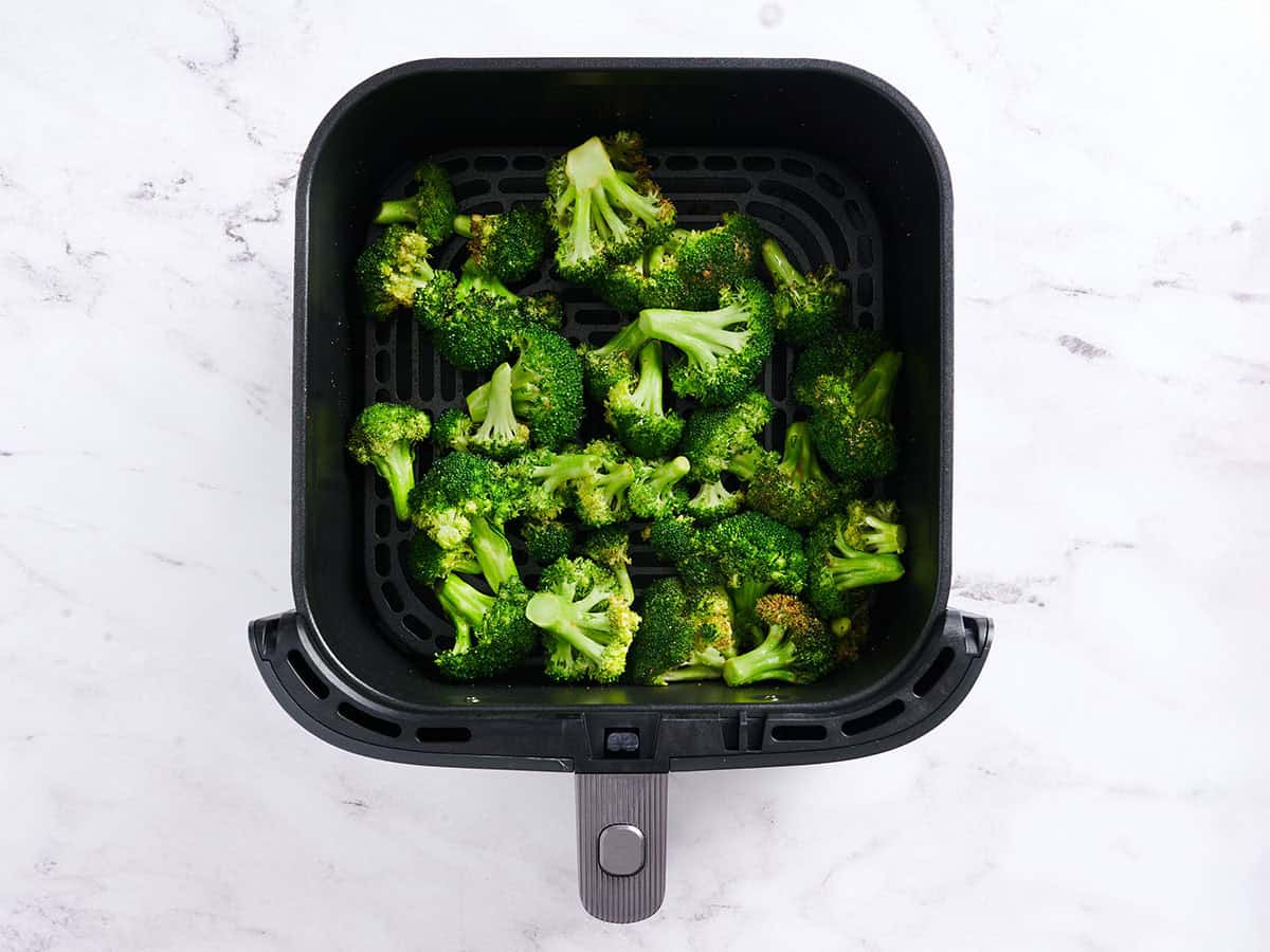 Broccoli florets in a air fryer basket after being shaken once during the cooking process.