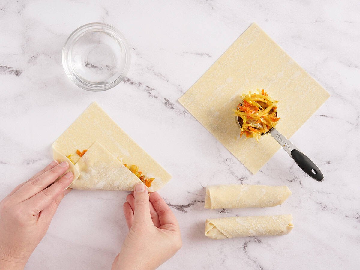 A hand rolling vegetable egg rolls.