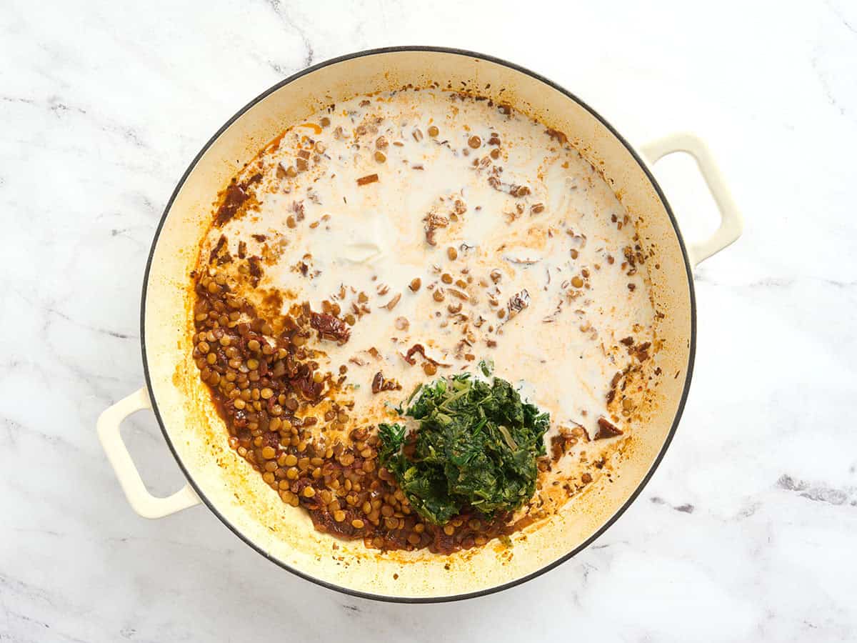 Cream and frozen spinach added to a pot for marry me lentils.