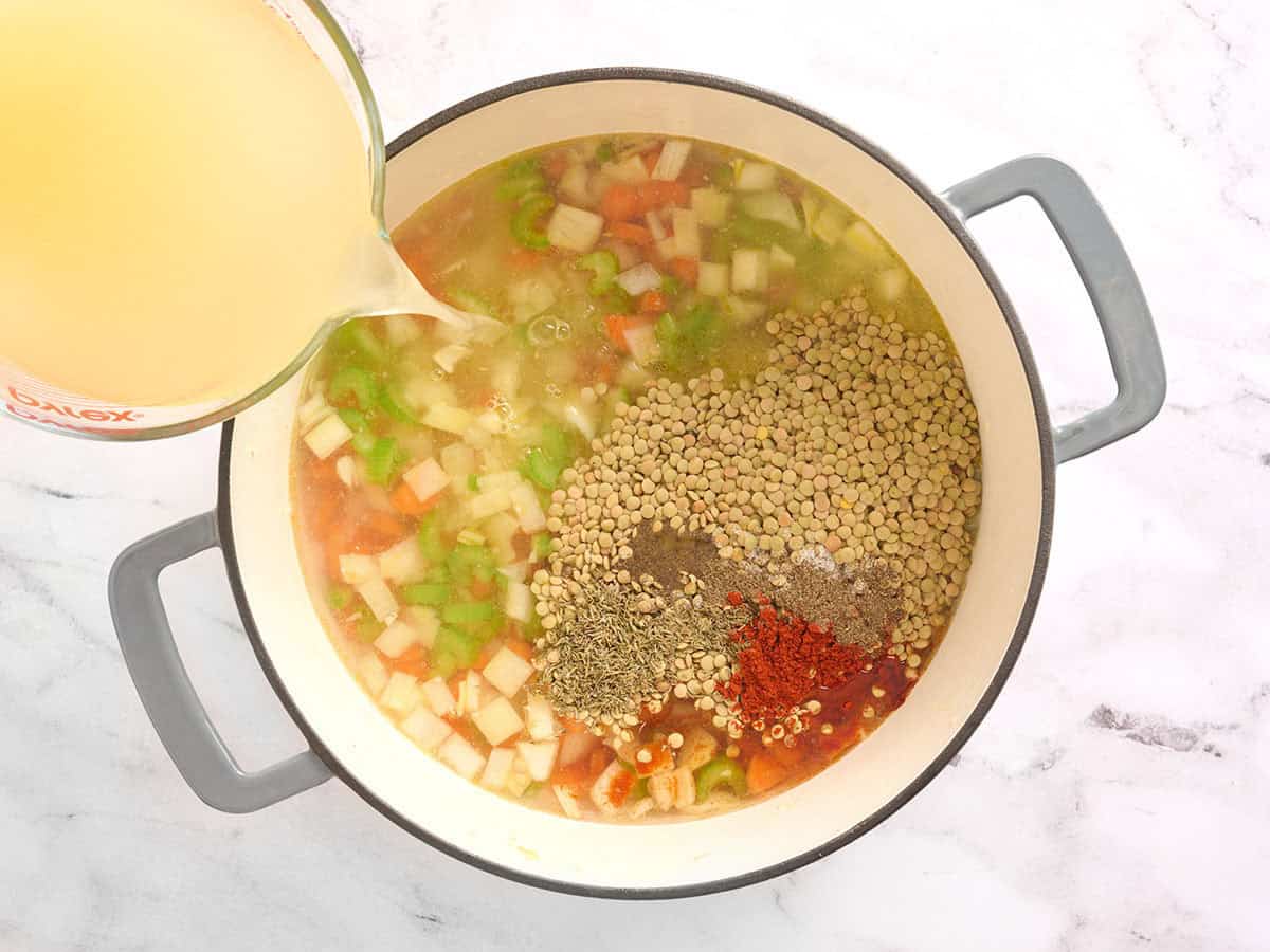 Dried lentils, seasonings, and broth added to a pot with vegetables.